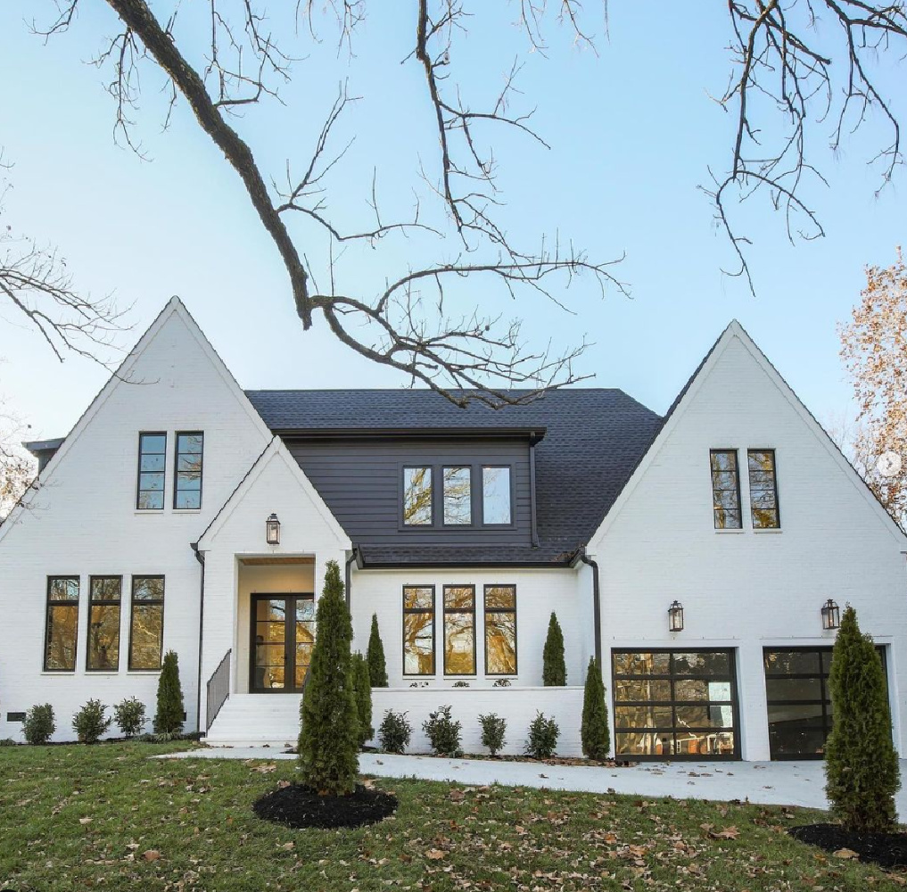 Modern white house with black trim and leafless trees.
