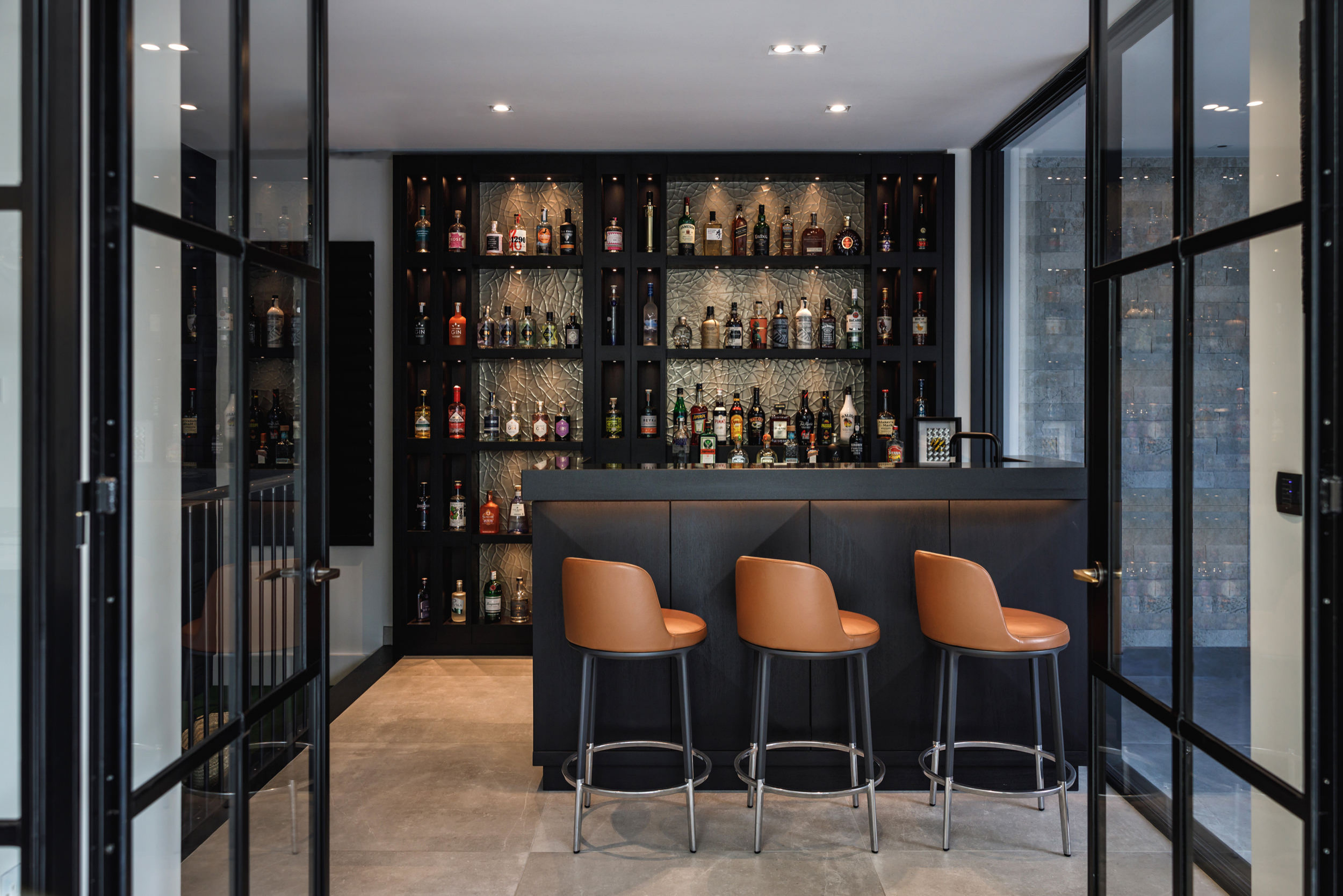 Modern bar interior with stools and shelves of liquor bottles.