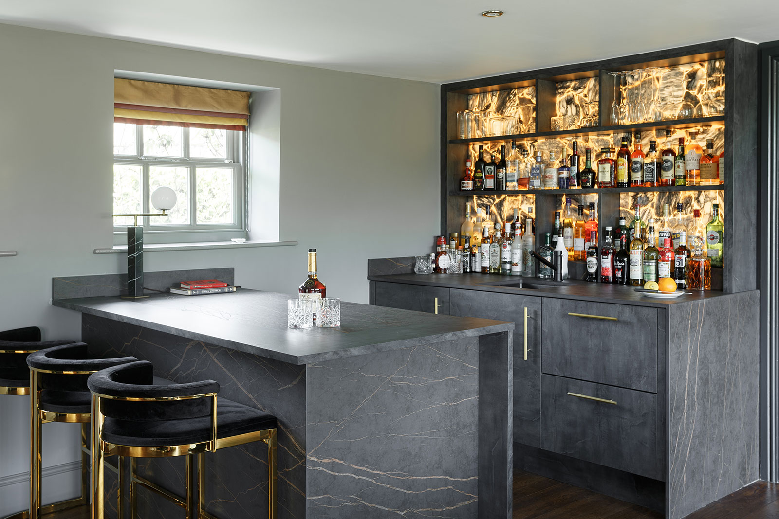 Elegant home bar with marble counters and shelves of liquor.